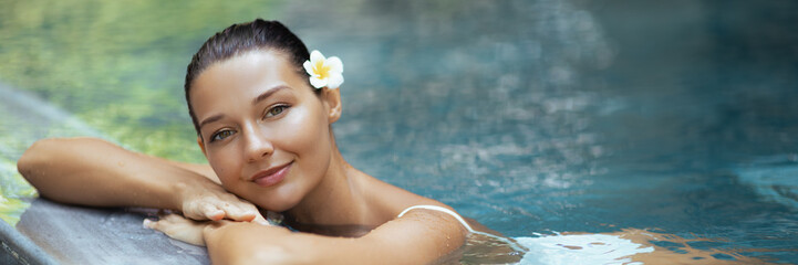 Woman Relaxing In Tropical Pool With Flower In Hair And Radiant Skin