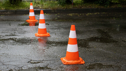 Traffic cones line a wet street, signaling a cautionary barrier during a rainy day at a busy...