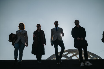 Four business people walking outdoors, silhouetted against sunlight, professional and confident.