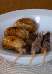 Grilled potatoes and beef skewers served on white plate