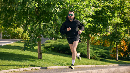 Person in sunglasses running outside through verdant foliage on a sunny day. Concept of physical...