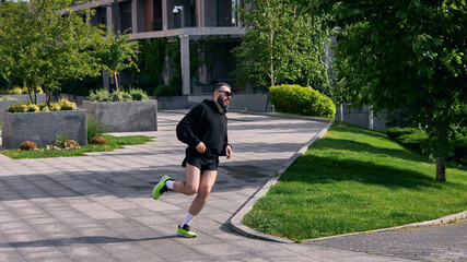 Middle aged man jogging in urban park under sunny sky near modern building. Concept of sportswear...