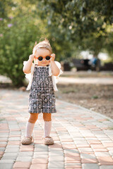 Smiling cute baby girl 2-3 year old wearing sun glasses and stylish summer clothes in park...