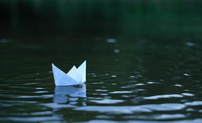 paper boat floating in water, abstract dark natural background. melancholy atmosphere image. symbol of travel, adventure, dreams. selective focus
