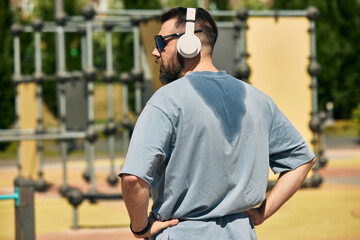 Man with headphones relishing exercise session at open-air fitness park. Concept of wearable tech,...