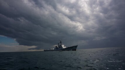 Navy vessel sails into bright horizon with dramatic clouds and sunlight breaking through