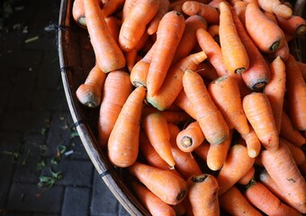 A collection of raw, fresh carrots placed on a wooden tray. The background is filled with vibrant orange carrots. This vegetable is rich in vitamin A and is beneficial for eye health.
