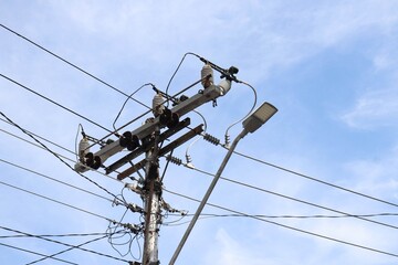 A utility pole carrying cables and a street lamp on a single pole stands against a clear blue sky....
