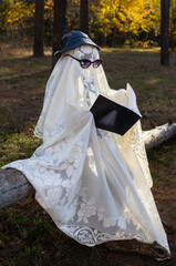 Funny Halloween photo. A child in a white blanket and black glasses sits in a forest or park and...