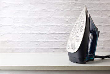 Steam iron on white wooden furniture and white brick background