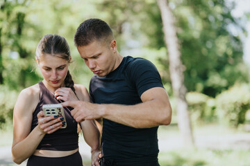A man and woman in athletic wear looking at a smart phone during a park workout.