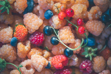 Colorful mix of fresh berries and fruits, including raspberries, strawberries, blueberries, and blackcurrants, showcasing a variety of textures and vibrant hues in natural light