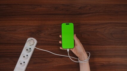 Hand Holding Charging Smartphone with Green Screen on Wooden Table