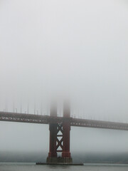 Close-up view of a Golden Gate Bridge pillar emerging from dense morning fog in San Francisco, with...