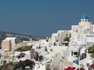 Fototapeta premium Iconic white houses with blue domes overlooking the Aegean Sea in Santorini, Greece. Traditional Cycladic architecture, bright sunlight, and a serene summer atmosphere in the Mediterranean.