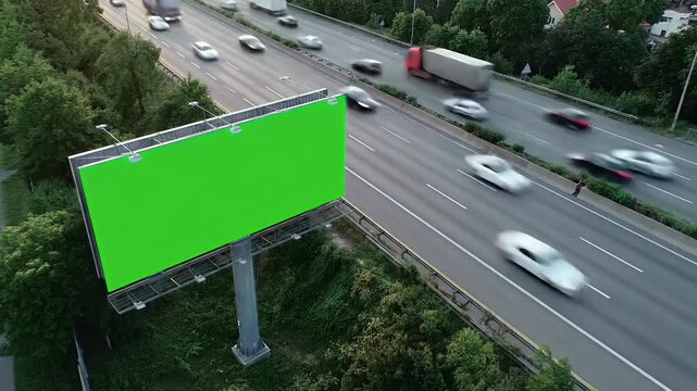 Aerial View of Green Screen Billboard Next to a Busy Highway with Motion Blurred Vehicles, Ideal for Advertising Mockups and Outdoor Promotions