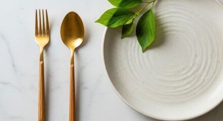 Elegant gold cutlery and a speckled ceramic plate adorned with fresh green leaves on a marble surface