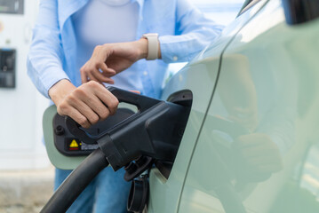 Close up of electric car driver looking at time on watch while waiting to charge electric car for...