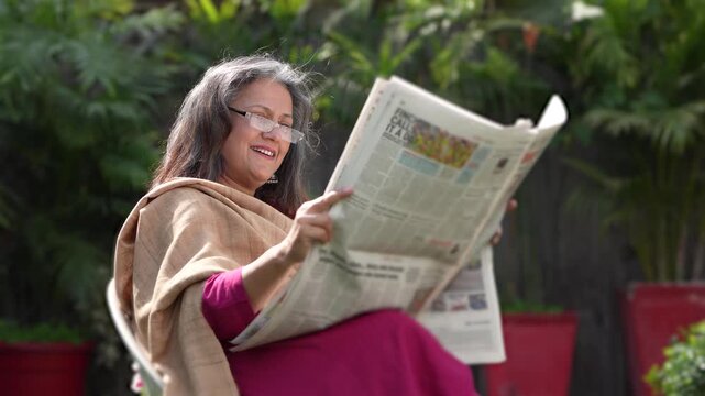 Relaxed senior woman sitting on chair at out of home reading newspaper.