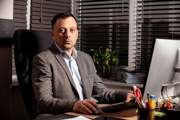 Confident businessman in a suit jacket working at a modern office desk. Sitting with a notebook and...