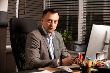 Confident businessman in a suit jacket working at a modern office desk. Sitting with a notebook and...