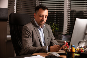 Confident businessman in a suit jacket working at a modern office desk. Sitting with a notebook and...