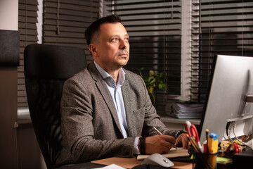 Confident businessman in a suit jacket working at a modern office desk. Sitting with a notebook and...