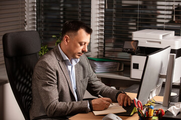 Confident businessman in a suit jacket working at a modern office desk. Sitting with a notebook and...