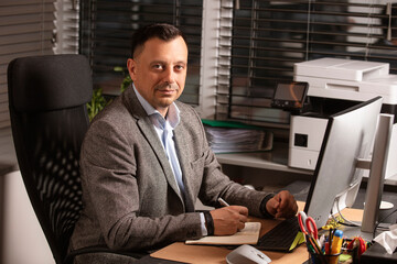 Confident businessman in a suit jacket working at a modern office desk. Sitting with a notebook and...