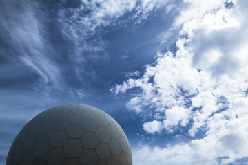 A modern radar spherical structure set against a vivid blue sky with clouds
