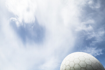 A modern radar dome structure set against a vivid blue sky with clouds