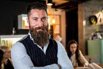 Portrait of a confident bearded businessman with arms crossed in a modern creative office. He wears a striped vest and exudes leadership, charisma, and professionalism. Millennial entrepreneur.