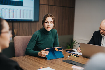 Three coworkers collaborate in a business meeting environment, using digital devices like tablets...