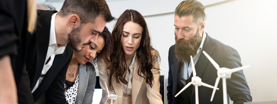 Team of professionals working together on wind energy project with turbine models. Business meeting focused on innovation, clean energy and sustainability. Renewable energy concept.