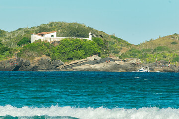 Beautiful view of Praia do Forte, with the sea around, many rocks, cloudy sky and mountain in the background.