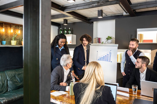 Diverse business team discussing growth strategy during a presentation in a modern office. Flipchart with bar graph shows increasing results. Corporate teamwork and project development concept. - Powered by Adobe