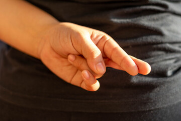 Hand discreetly crossing fingers behind the back, symbolizing good luck, hope, or perhaps dishonesty and a white lie. Concepts of superstition, promises, secrets, or truthfulness.