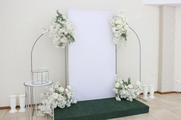 Indoor white wedding photo area decorated with flowers.