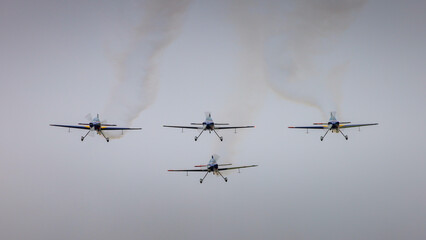 Four acrobatic airplanes fly in perfect formation, seen from the front against a dark sky.