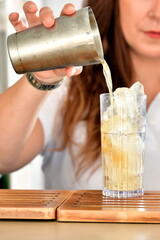 Mano che versa un cocktail in un bicchiere colmo di ghiaccio – bevanda fresca in preparazione, ideale per l’estate, momenti di relax e aperitivi rinfrescanti