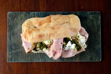 Panino farcito con mortadella e mozzarella, servito su tagliere in pietra . Semplice e gustoso, ideale per uno spuntino veloce o un pranzo informale. Foto vista dall’alto.