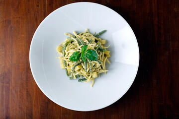 Piatto di trofie al pesto di basilico, condite con olio d’oliva e una spolverata di parmigiano. Specialità ligure servita su fondo rustico, fotografata dall’alto.