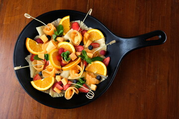 Colorata e fresca macedonia di frutta mista servita in una ciotola nera, perfetta per un dessert leggero e salutare. La combinazione di fragole, kiwi, ananas, uva e mela 