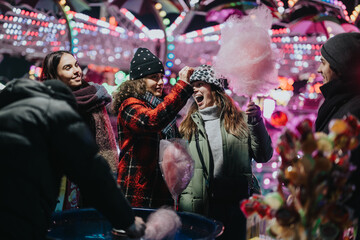 A group of friends share joyful moments while enjoying cotton candy at a vibrant winter fair...