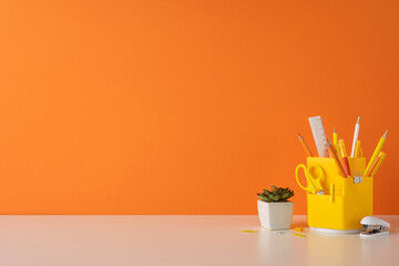 Vivid orange background with a white desk furnished with stationary essentials and a plant to...