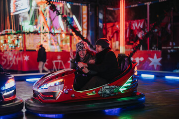 A group of friends have fun driving bumper cars at a festive winter amusement park. The image...