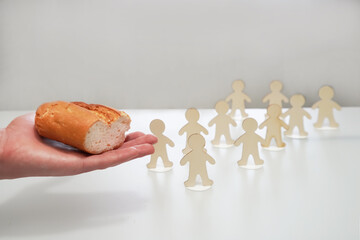 Hand extends or gives a piece of bread to the figures of people. Inequality in society, limited access to food, helping the hungry, charity Management, power, manipulation, dependence provoking hunger