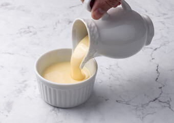 Hand pouring condensed milk in a bowl over marble background