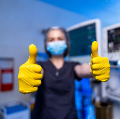 Healthcare worker thumbs up. A masked healthcare worker in yellow gloves gives a thumbs up,...