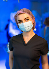 Clinical healthcare worker. A healthcare worker in scrubs and a mask stands confidently in a...